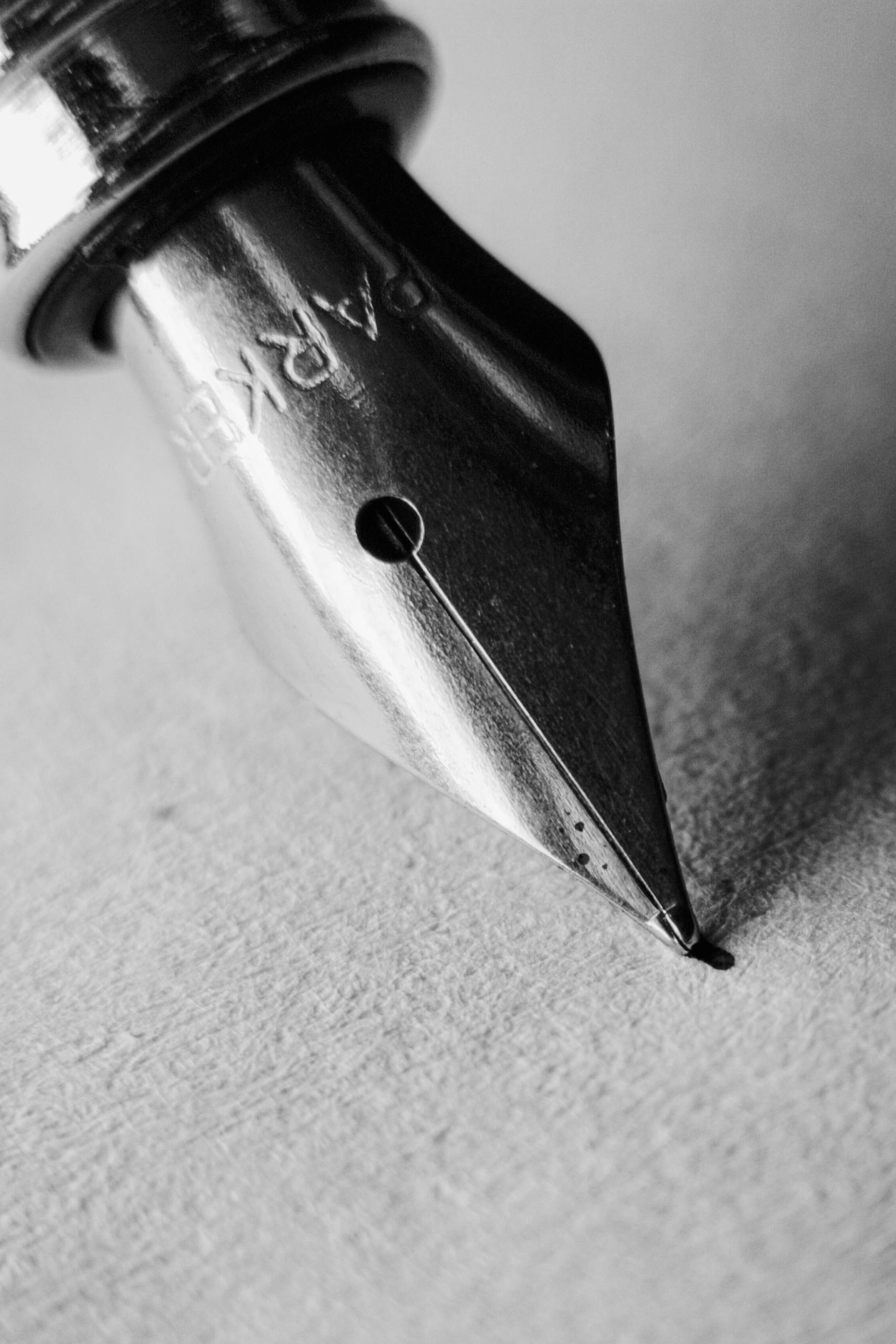 Detailed black and white close-up of a fountain pen nib on textured paper.