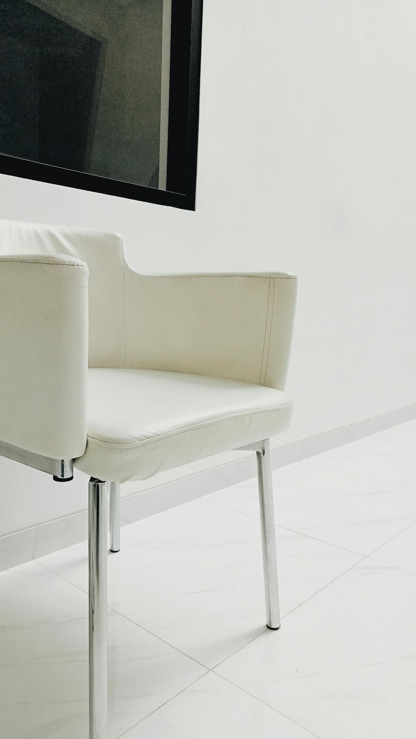 Modern white leather chair with chrome legs in a minimalist room, featuring a glass window.