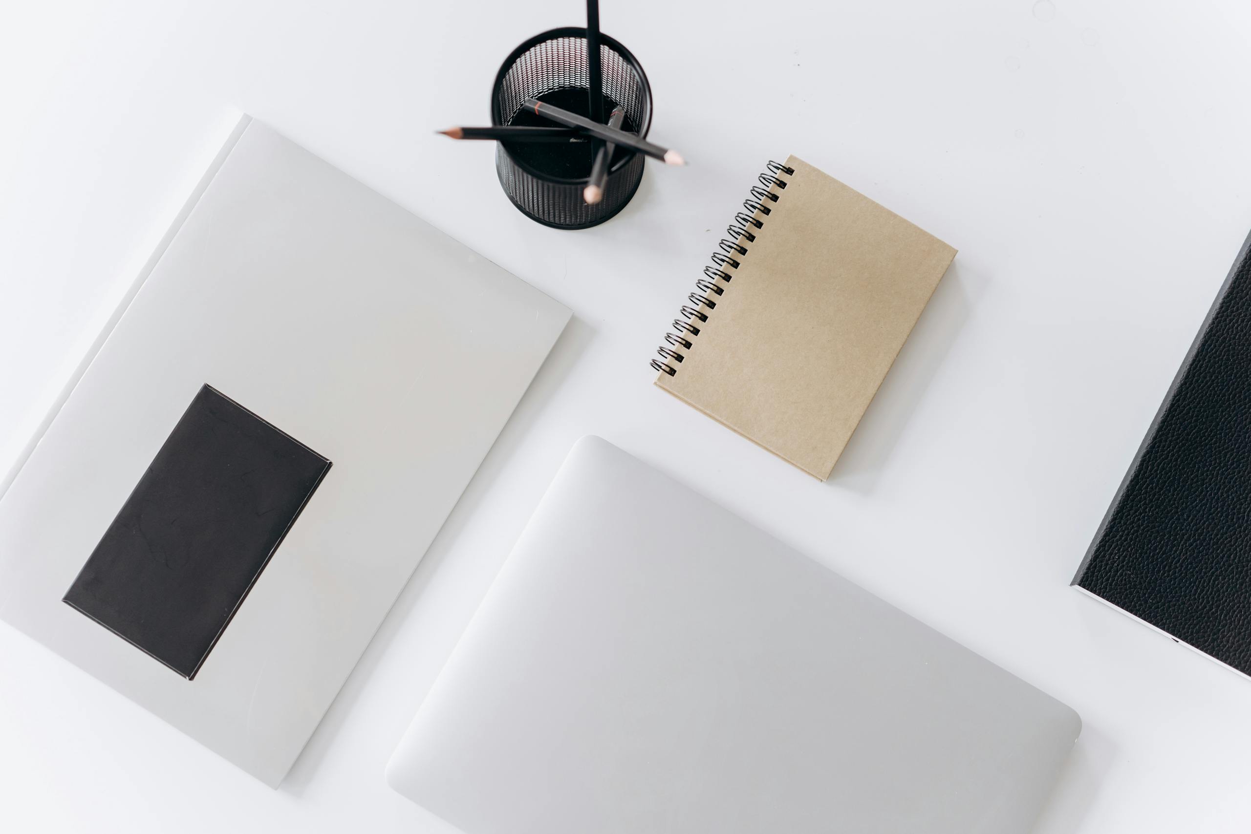 Top view of modern laptop with notebooks and cup of pencils composed on white table in office